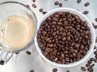 Roasted coffee beans in white bowl with americano in glass cup on table