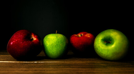 red and green apples on a wooden board on a black background. front view