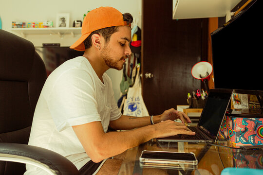 Joven gay con gorra color naranja utilizando su laptop en su habitación