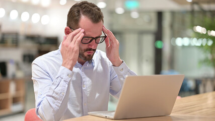 Stressed Businessman with Laptop having Headache in Office