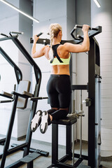 Blonde attractive slim woman wearing sport bra do exercises pull-ups on the horizontal bar in...