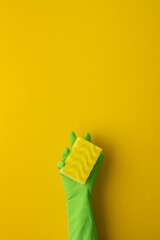 A hand in a green protective rubber glove holds a washing sponge on a yellow background