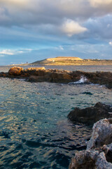 Obraz premium Beautiful ocean water with light from the setting sun hitting the hill in the background at Qawra, Malta.