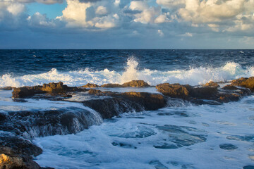 Light shining on the water as it splashes over rocks in the ocean at Qawra, Malta on a fall evening.