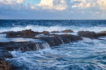 Water over rocks in the blue ocean at sunset in Qawra, Malta.