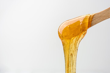 Liquid yellow sugar paste or wax for epilation on wooden stick or spatula closeup - obrazy, fototapety, plakaty