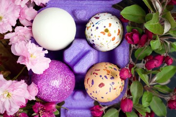 Obraz na płótnie Canvas Four eggs decorated with wax and glitter in a purple egg wrapper and branches of ornamental cherries.