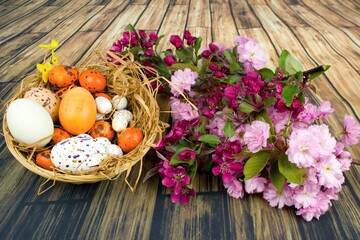 Color eggs decorated with wax and glitter in a basket and branches of ornamental cherries.