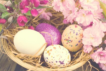 Naklejka na ściany i meble Color eggs decorated with wax and glitter in a basket and branches of ornamental cherries.