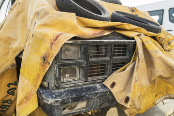 Closeup of an old rusty pickup truck covered with a yellow tarpaulin