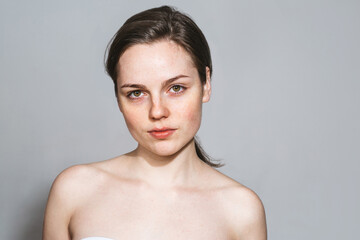 Young beautiful freckles woman face portrait with healthy skin. Gray background.