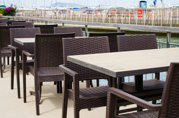 Wicker tables and chairs on the terrace of a cozy summer cafe overlooking the water.