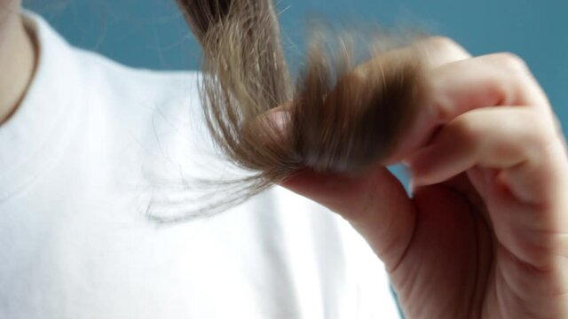 Girl holding her hair with split ends in her hands close-up on blue background.