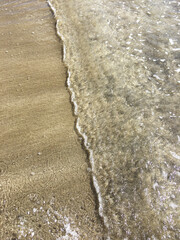 Waves crashing on sandy beach shore with small ripple texture. Clear, crisp ocean water.