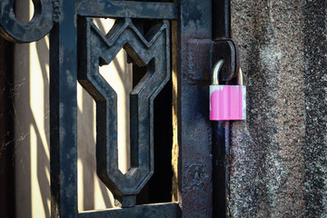 Pink painted padlock hanging on black iron fence