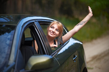 Young woman in the car with her head in the window and with her hand raised