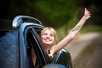 Young woman in the car with her head in the window and with her hand raised