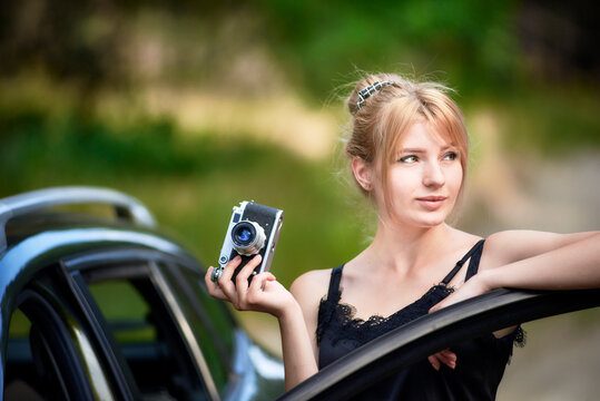 Young beautiful woman takes pictures leaning on the open front door of her car