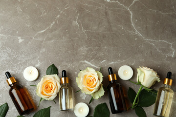 Bottles with rose essential oil, roses and candles on gray textured background