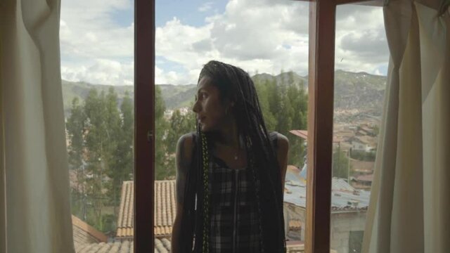 Mujer transgénero con trenzas observa el paisaje a través de su ventana 