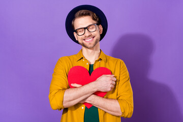 Photo of cheerful happy young man adore hold heart shape red paper hug isolated on purple color background