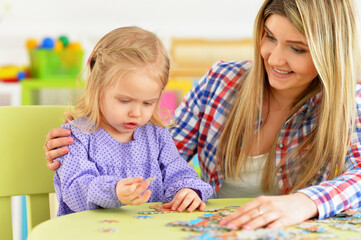 Fototapeta premium Mother with little daughter collecting puzzle