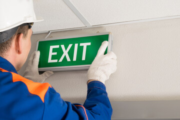 the hands of the foreman install emergency exit lighting - obrazy, fototapety, plakaty