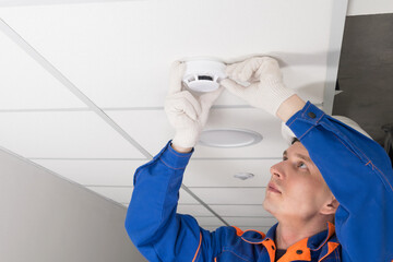 a worker installs a smoke and fire detector on the ceiling in the office, close-up