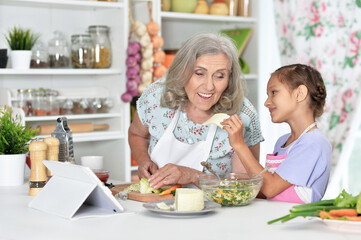 Cute little girl with her grandmother cooking together at kitchen table