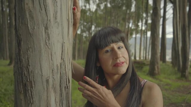 Mujer transgénero posando apoyada de un árbol en el bosque 