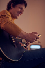 Male musician playing acoustic guitar on the amplifier in retro vintage room.