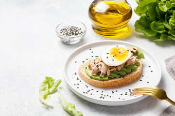 Obraz na płótnie Canvas Avocado, canned tuna and boiled egg toast on white stone table background. Healthy food, avocado open sandwich for breakfast or lunch. Close up, copy space