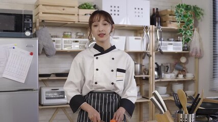 female chef recording video for her channel at home kitchen while prepping for food with knife. looking at camera, asian woman vlogger sharing cooking tips on social media with hand gesture.