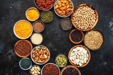 Selection of superfoods, legumes, cereals, nuts, seeds in bowls on black background. Superfood as chia, spirulina, beans, goji berries, quinoa, turmeric and other. Copy space, top view