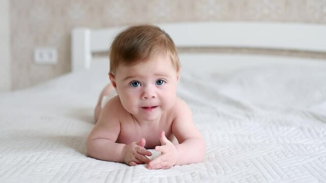 Cute little baby boy lying on stomach on the bed, learning to hold the head. Portrait of a nice newborn baby in diaper looking interestingly at camera with his mouth open.