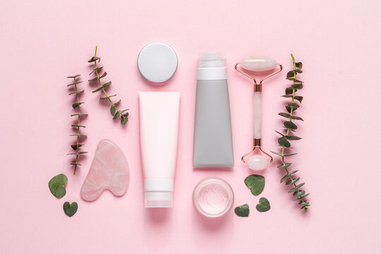 Set of cosmetic products for the face and body. Face roller, guasha massager, cream jar, plastic tube on pastel pink background. Facial care beauty products