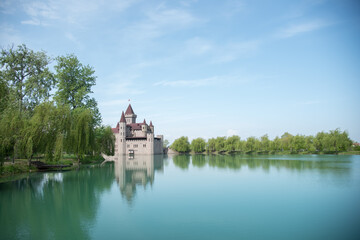 Fototapeta na wymiar Kabardino-Balkarian Republic, Russia, Chateau Erken, 05/01/2021 Castle on the water, bright blue water and sky. Reflection of a modern castle in the water. Tower. Willows on the shore.