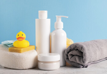 Obraz na płótnie Canvas Bath accessories for kids on light blue background. Yellow rubber duck, shampoo bottle, cosmetic milk and cream, soap, sponge, towel on table. Hygiene, natural skincare concept