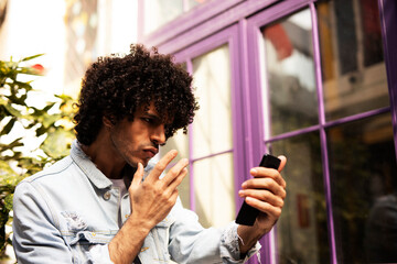 Young man enjoying outdoors. Handsome man with curly hair using the phone, having video call...