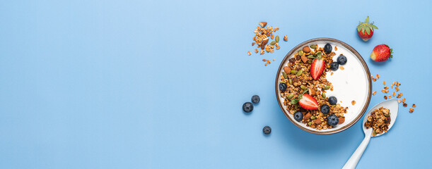 Healthy breakfast with homemade granola, berries and greek yogurt. Oatmeal, nuts, strawberries and blueberries in bowl on bright blue background. Copy space, top view