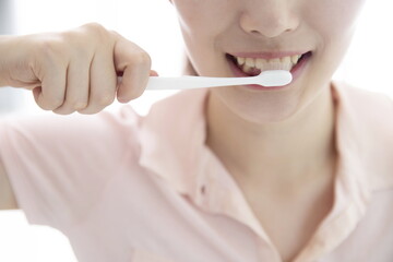Smiling young woman brushing teeth, cropped