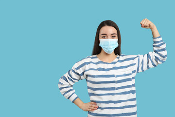 Woman with protective mask showing muscles on light blue background, space for text. Strong...