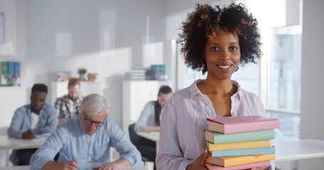 Portrait of african teacher holding text books and smiling at camera in classroom