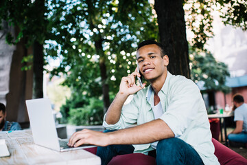 Content young black man talking on smartphone while working on laptop
