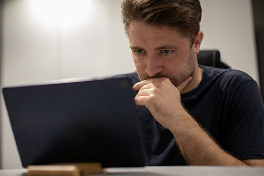 Close Up Portrait Of Focused Unshaven Handsome Guy Looking At Tablet Screen, Working From Home Remotely, Participating In Online Conference At White Interior. Male Staying Connected During Pandemic