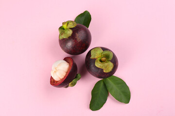 Fresh ripe mangosteen fruits with green leaves on pink background, flat lay