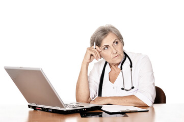 Serious elderly woman doctor sitting at table with computer Serious elderly woman doctor sitting at table with computer