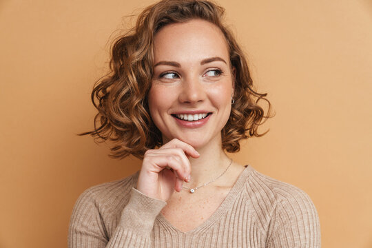 Young ginger woman with wavy hair smiling and looking aside