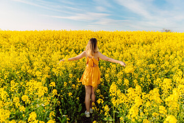 Naklejka na ściany i meble Attractive woman in blooming rapeseed field with sunset light. Yellow flowers and happy woman