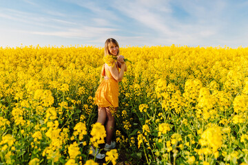 Naklejka na ściany i meble Portrait of attractive woman on blooming rapeseed field with sunset light. Yellow flowers and happy woman
